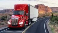 Peterbilt Model 579 Class 8 Heavy Duty Day Cab hauling a box trailer on curved road in front of red rocks - Thumbnail